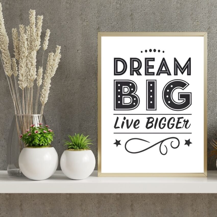 A Dream Big, Live Bigger framed wall art sits on a white shelf beside two white vases against a gray textured wall.