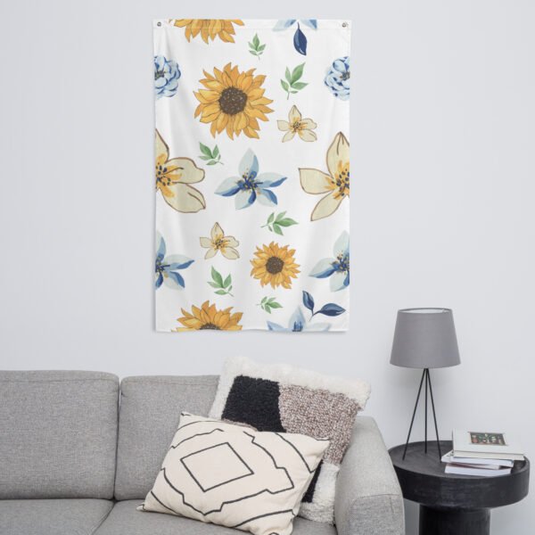 A Sunflower pattern tapestry wall hanging hangs above a gray sofa with a geometric pillow. Next to the sofa is a black side table holding books and a gray lamp.