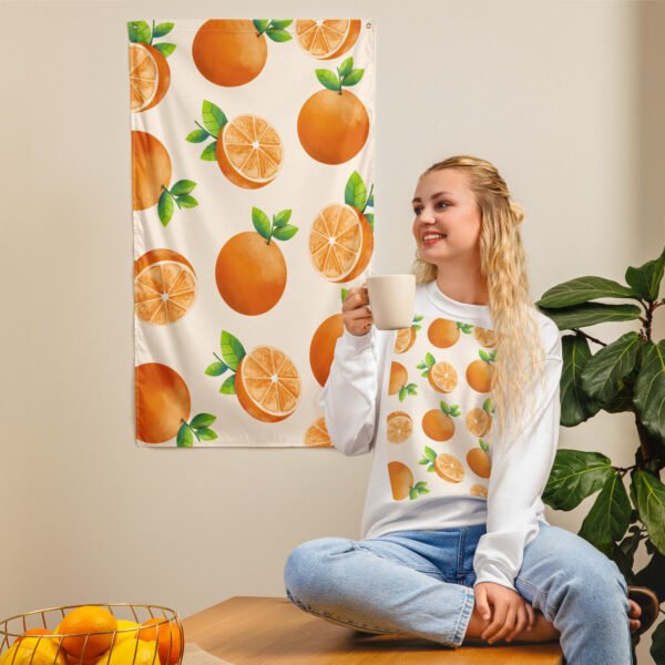 Orange fruit pattern tapestry wall hanging displayed as wall art behind her. A bowl of oranges and a green plant are nearby.