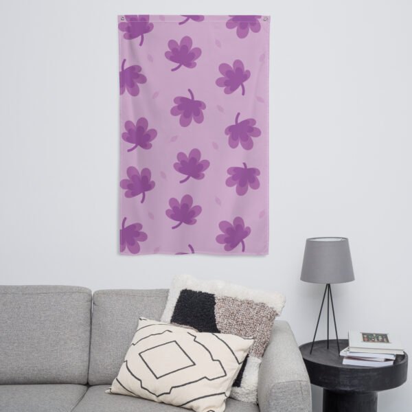 The Purple leaf pattern wall tapestry in light purple with darker purple leaves hangs above a gray sofa with cushions; a round black table, lamp, and books sit nearby against the white wall.