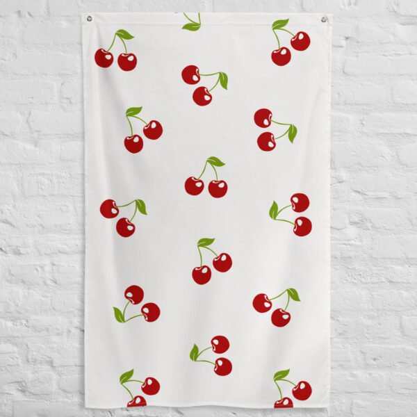 The Cherry pattern tapestry is a white cloth featuring a repeating design of pairs of red cherries with green stems and leaves, shown hanging against a white brick wall.