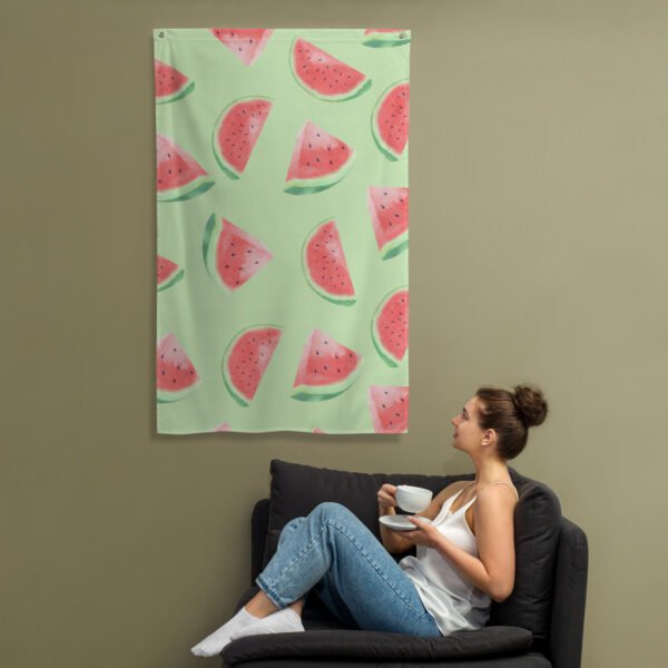 A woman on a dark couch holds a cup and saucer, gazing up at the Watermelon pattern tapestry featuring playful watermelon slices on a light green background.