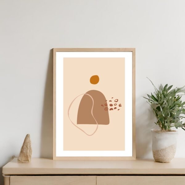 Abstract artwork featuring shapes in earthy tones, framed and displayed on a wall with a plant nearby.