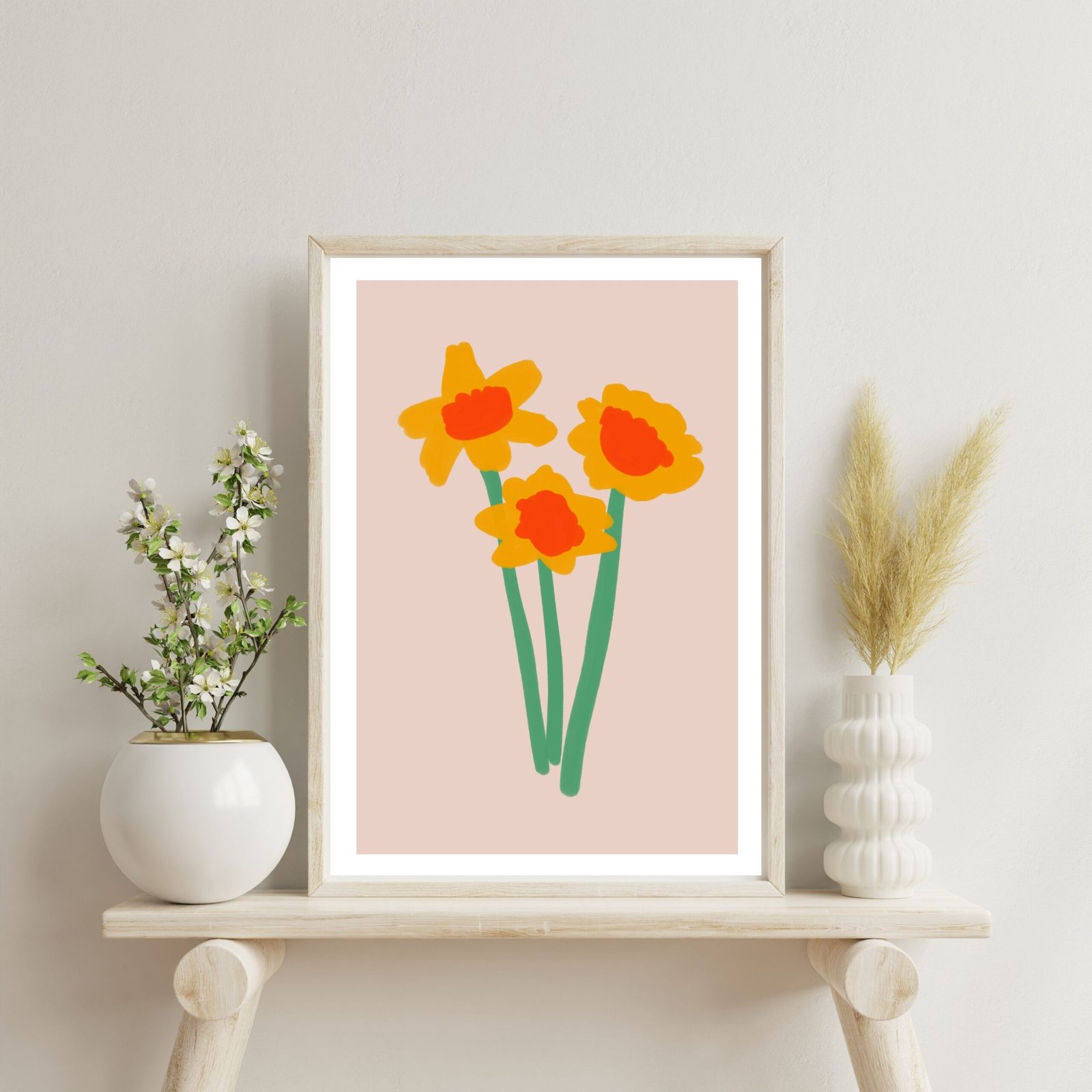 Framed artwork featuring three daffodils with orange centers and green stems against a light pink background.