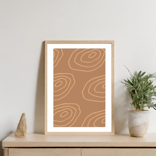 Framed abstract artwork featuring brown and beige circular patterns displayed on a wall.