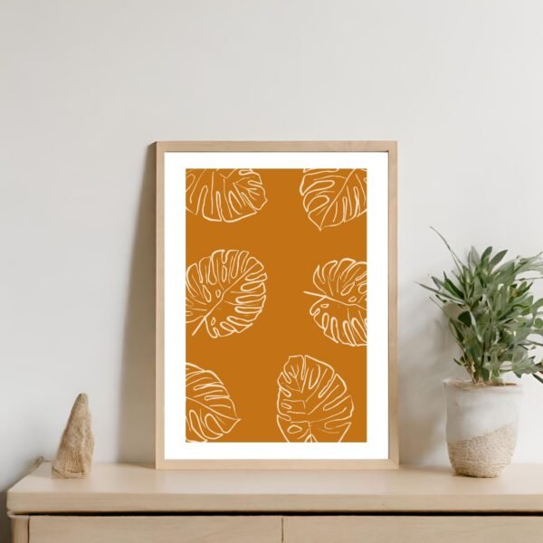 Framed artwork featuring Monstera leaves on an orange background in a simple wooden frame.