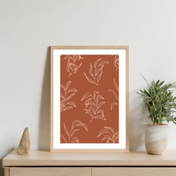 Framed artwork featuring leaf patterns on a brown background displayed on a shelf.