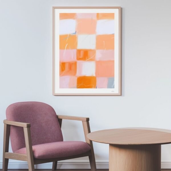 Framed abstract artwork featuring orange and pink blocks displayed on a wall next to a chair and table.