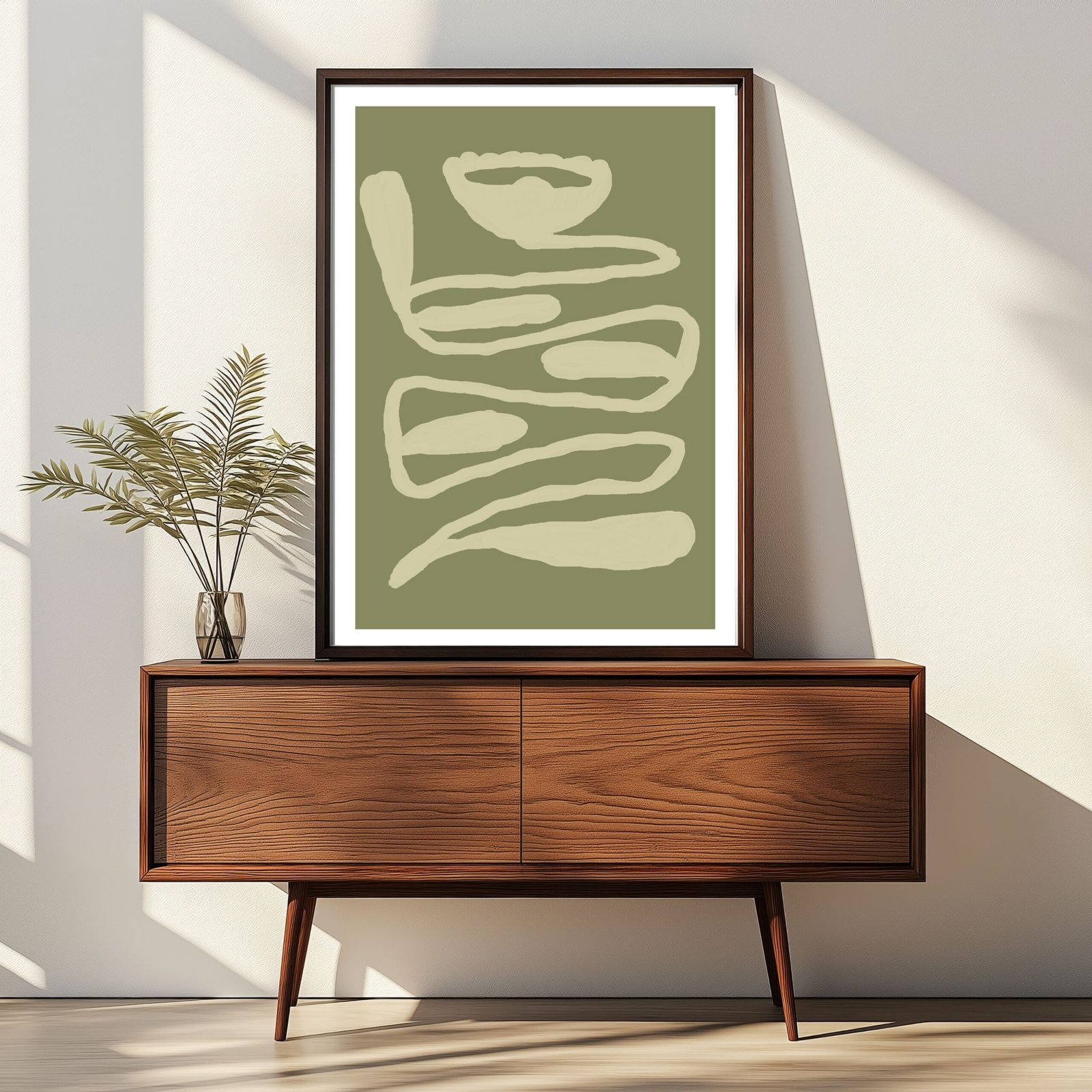 Framed abstract artwork featuring curved lines in muted green and beige colors displayed on a wooden cabinet.