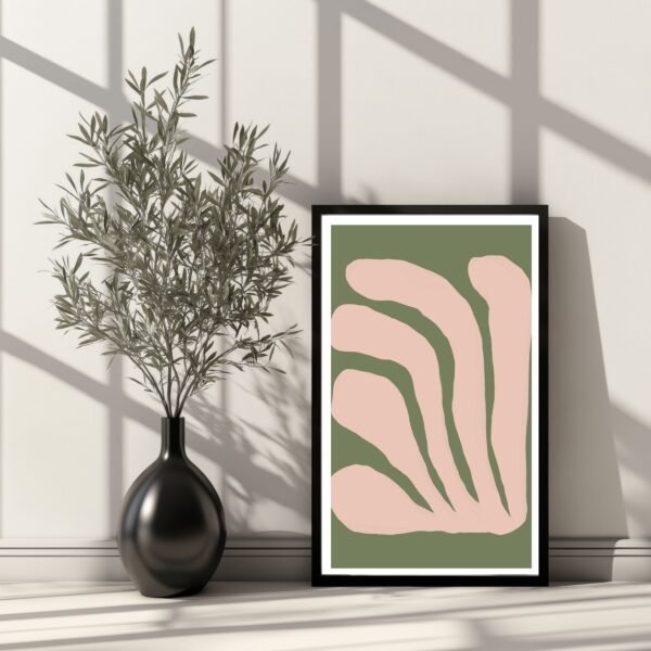 Framed abstract artwork featuring organic shapes in pink and green colors displayed next to a plant in a vase.